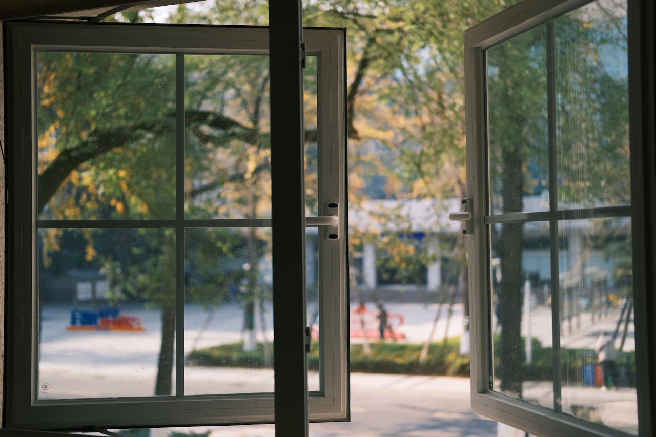 A serene view through an open window, showcasing green trees and bright light, capturing a tranquil outdoor scene.